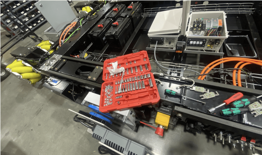 A workbench setup with an open toolbox containing various tools laid out neatly, amidst other electrical equipment and wiring of a large parking robot.