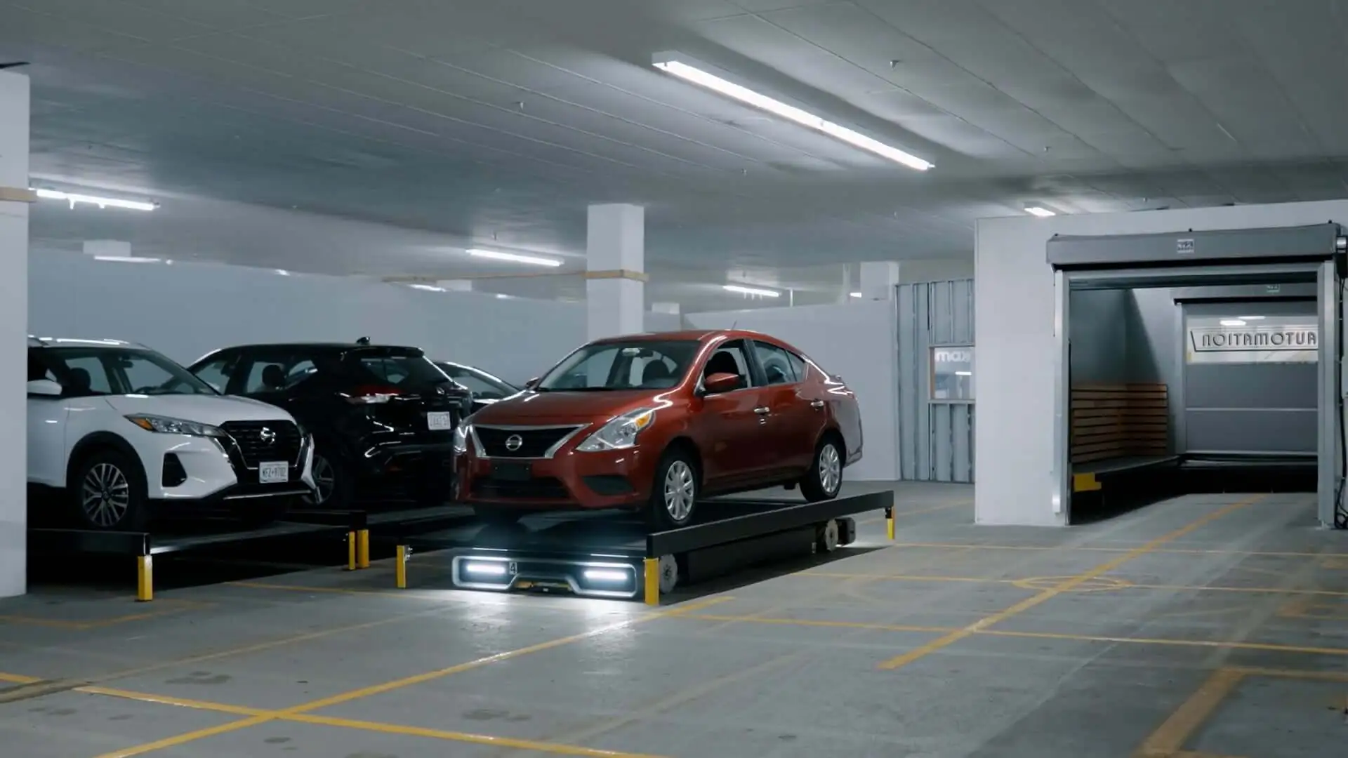 A bright underground parking garage with several cars parked. A red sedan is highlighted on an illuminated platform, being taken to its parking spot by a mobile robot.