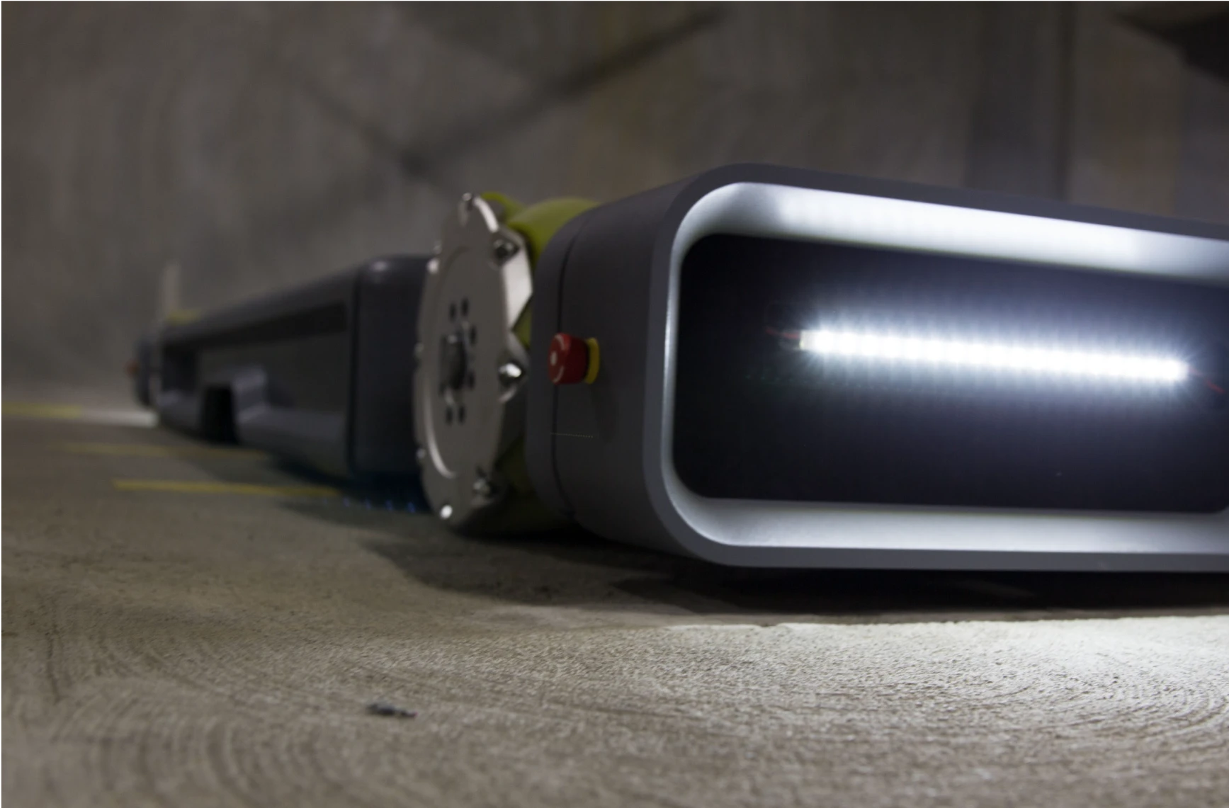 Close-up of an electric autonomous car parking robot, shown from a low angle in a parking garage, focusing on the front of the robot with lights illuminated.