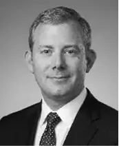 Black-and-white professional headshot of a man in a suit and tie, facing forward and smiling slightly. The background is plain and neutral.