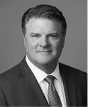 Black and white portrait of a middle-aged man in a suit and tie, facing forward and smiling slightly, with short, neatly styled hair, against a plain background.