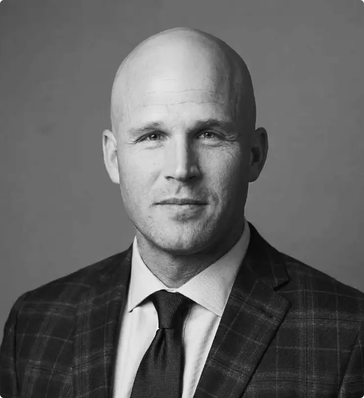 A bald man in a plaid suit jacket, dress shirt, and tie poses for a formal portrait against a plain background. The photo is in black and white.