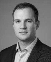 Black and white portrait of a man in a suit jacket and collared shirt, facing the camera with a neutral expression against a plain background.