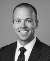 Black and white headshot of a smiling man wearing a suit and tie, with short hair, posing against a plain background.