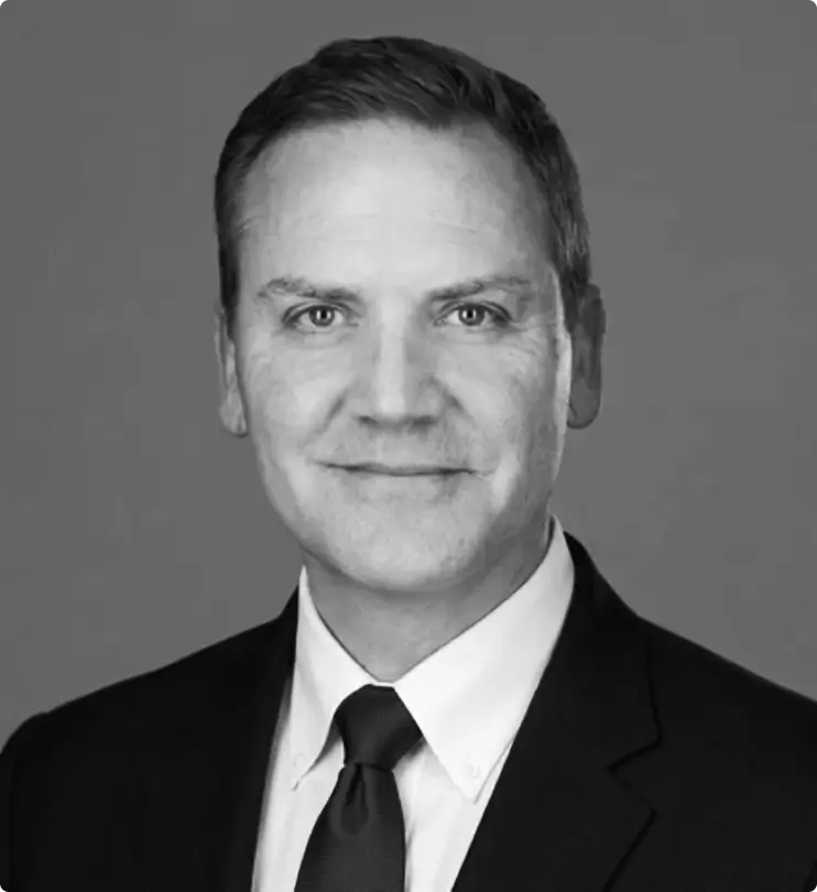 Black and white portrait of a man in a suit and tie, smiling slightly, with short hair, against a plain background.