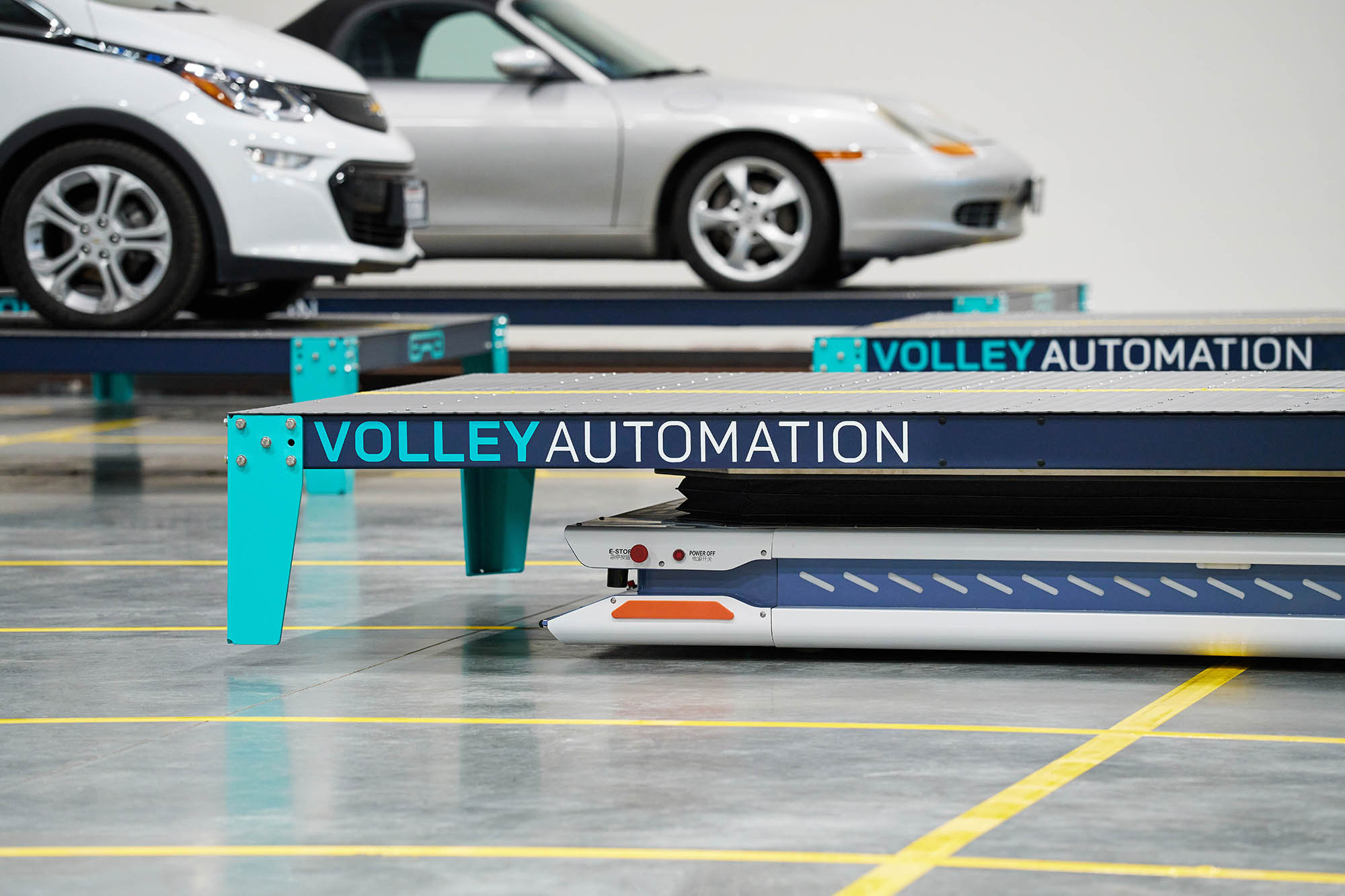 Four men work at computer stations in an industrial office, representing the dynamic environment of Careers at Volley Automation. Two type on keyboards, while one looks at a phone held by a standing colleague. Cables, monitors, and colorful desk toys are visible throughout the workspace.