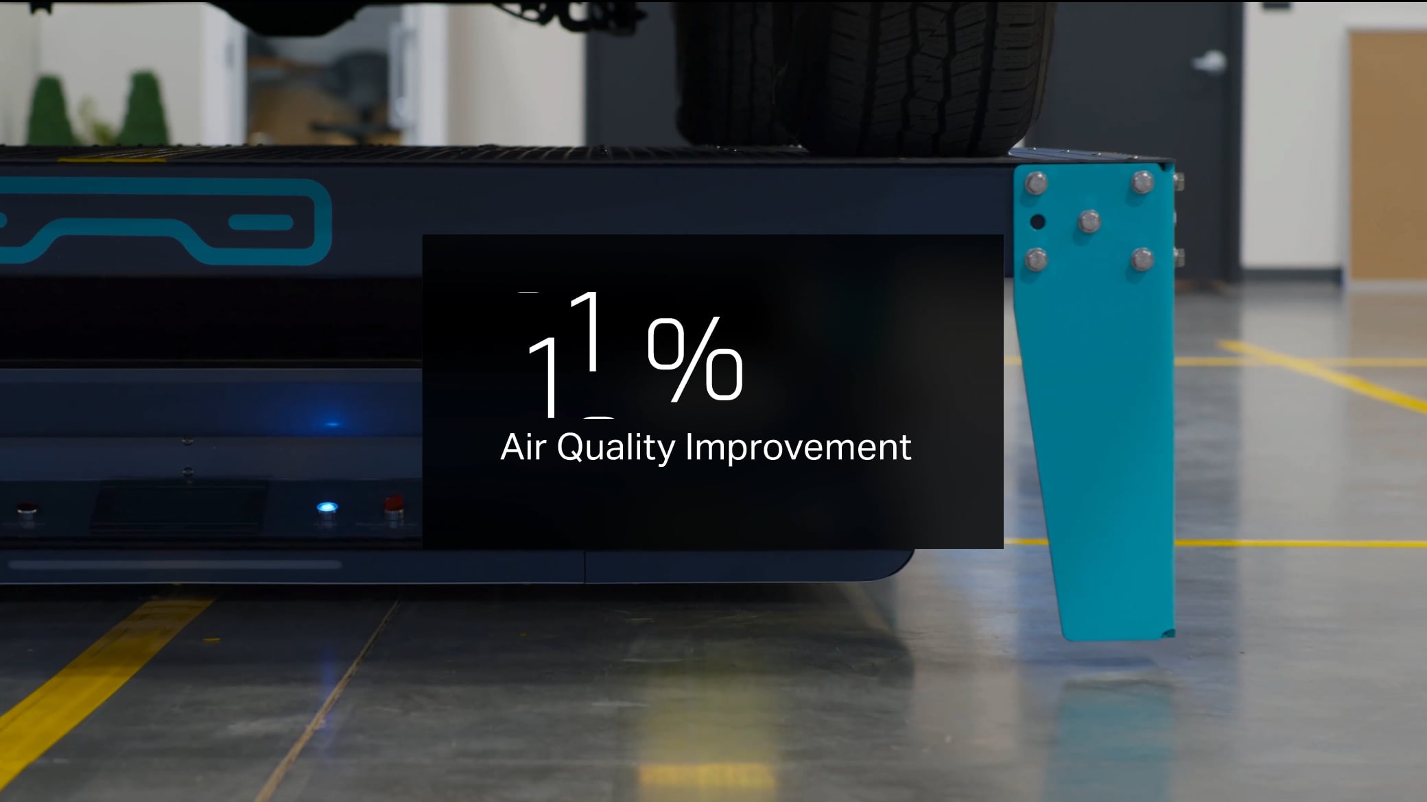 Close-up of industrial equipment next to a tire, with a screen overlay showing “1% Air Quality Improvement” in white text. The setting appears to be a clean, modern industrial or automotive facility—illustrating exactly why customers choose Volley Automation for innovative, efficient solutions.