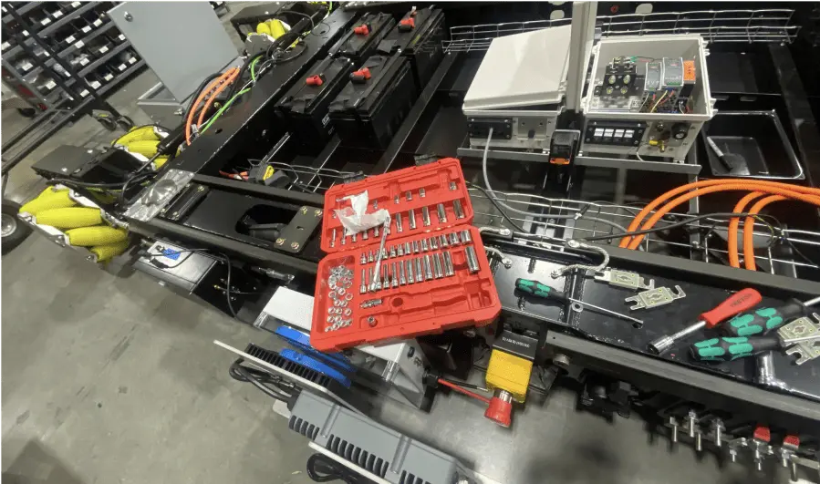 A red socket wrench set sits on a metal assembly surrounded by batteries, cables, electrical components, and various tools in a workshop or industrial setting—perfect for those working with Volley Automation.