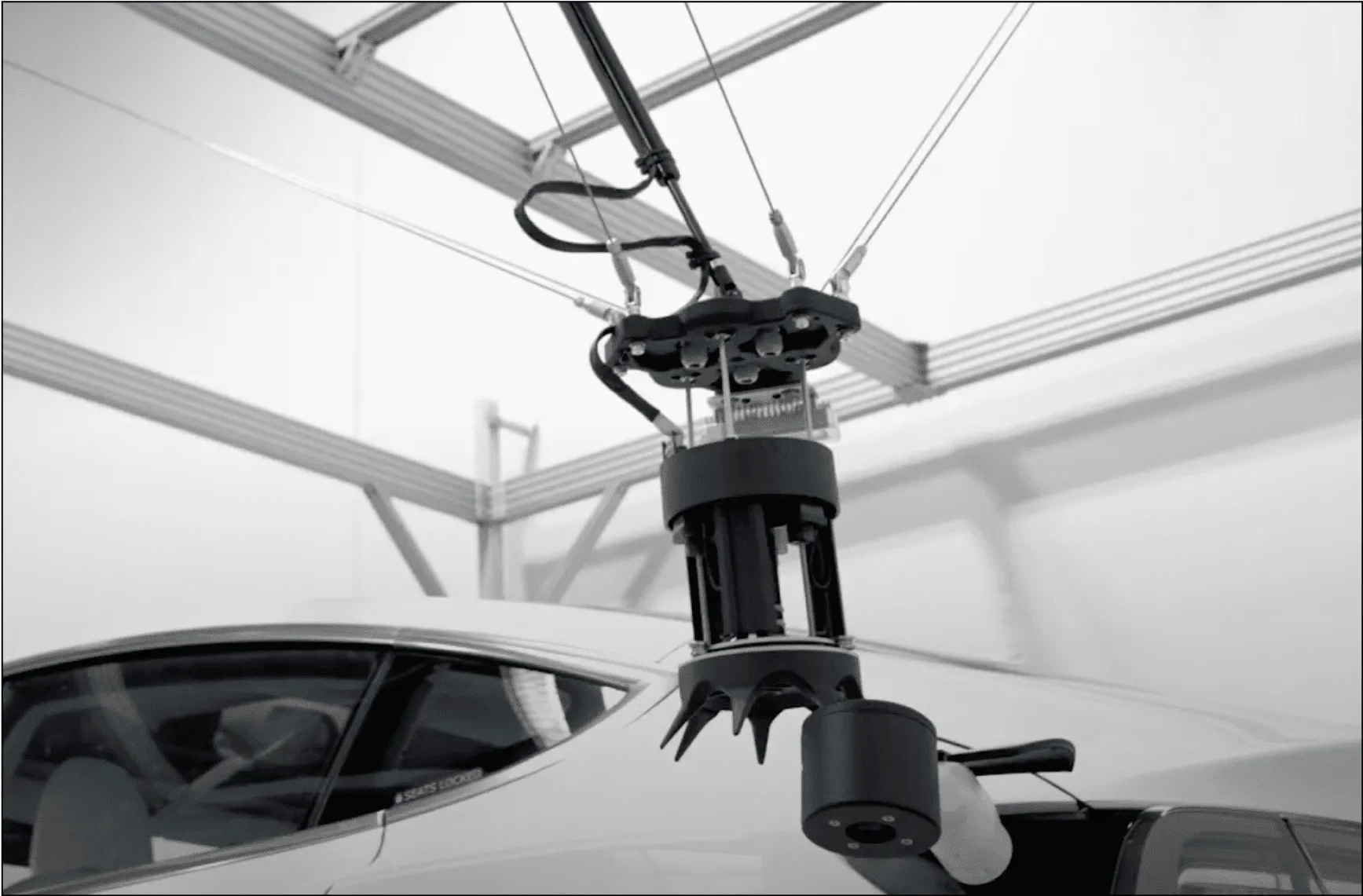 A robotic arm with a complex gripper hovers above the roof of a white car in a modern industrial setting, offering an impressive glimpse into how automated parking systems work.