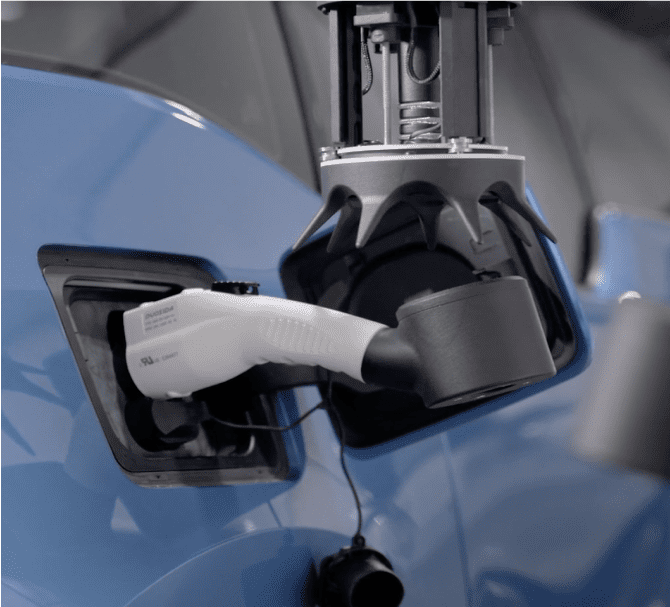 A robotic arm is inserting an electric vehicle charging connector into the charging port of a blue car, showcasing the precision and innovation that explain why choose Volley Automation for advanced automated solutions.